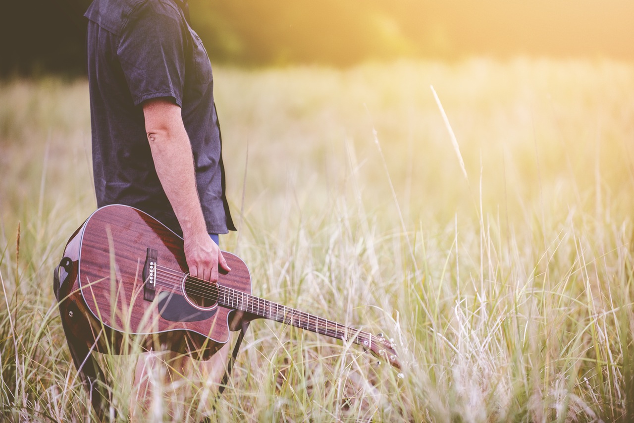 Man with guitar in field of tall grass.